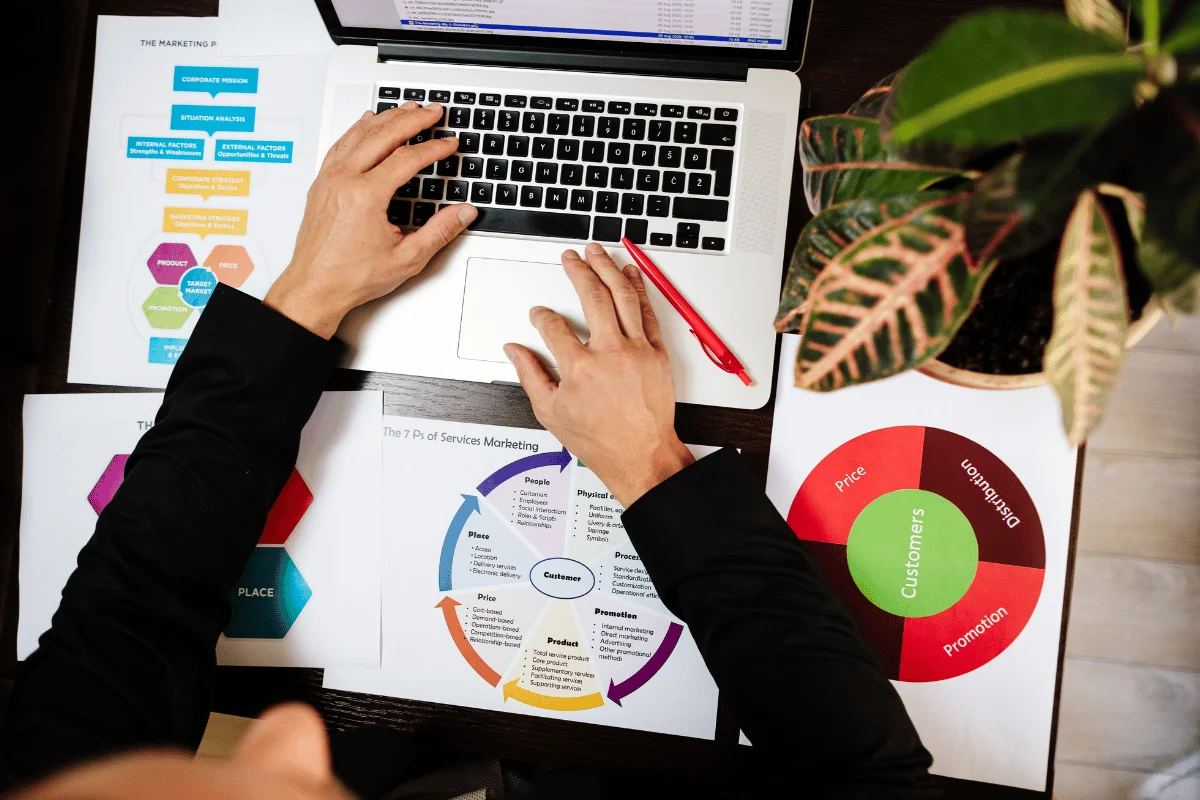 Person working on laptop with marketing strategy documents and colorful graphs.
