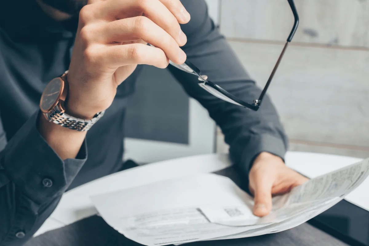 Person holding glasses above document on desk, wristwatch visible.