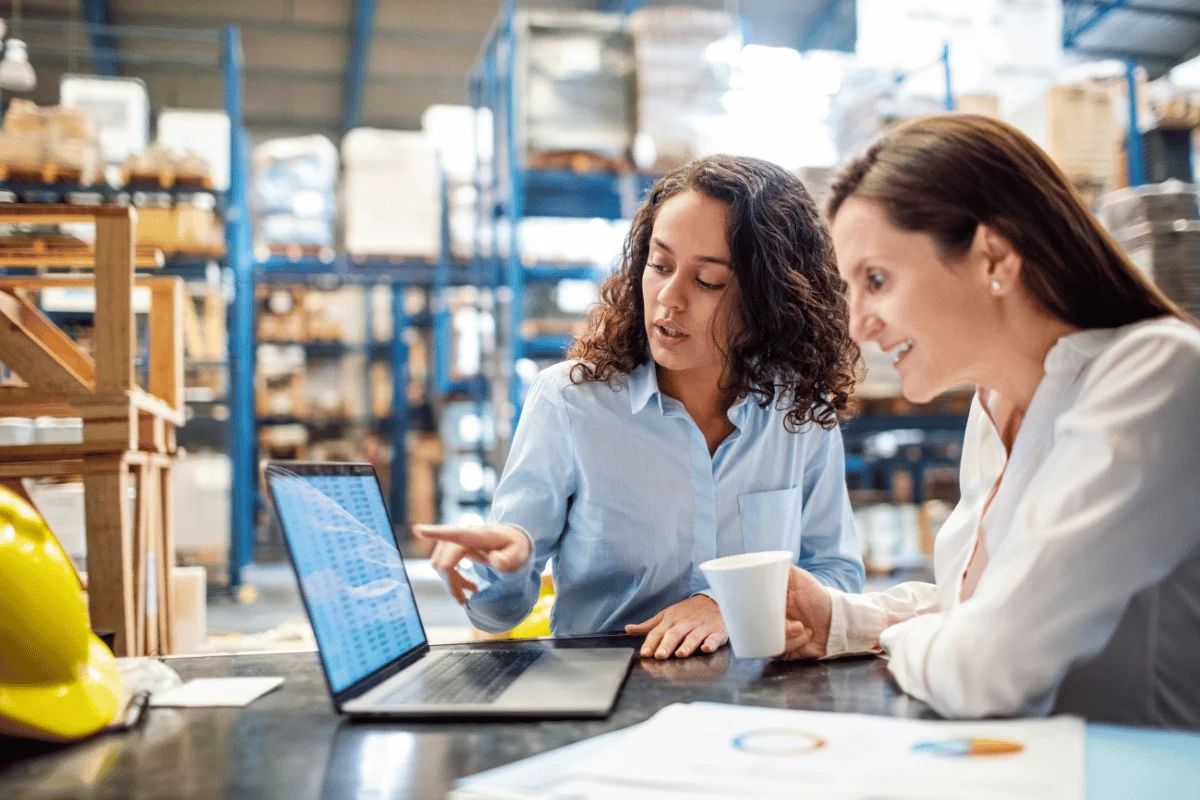 Warehouse employees collaborating and reviewing data on a laptop.