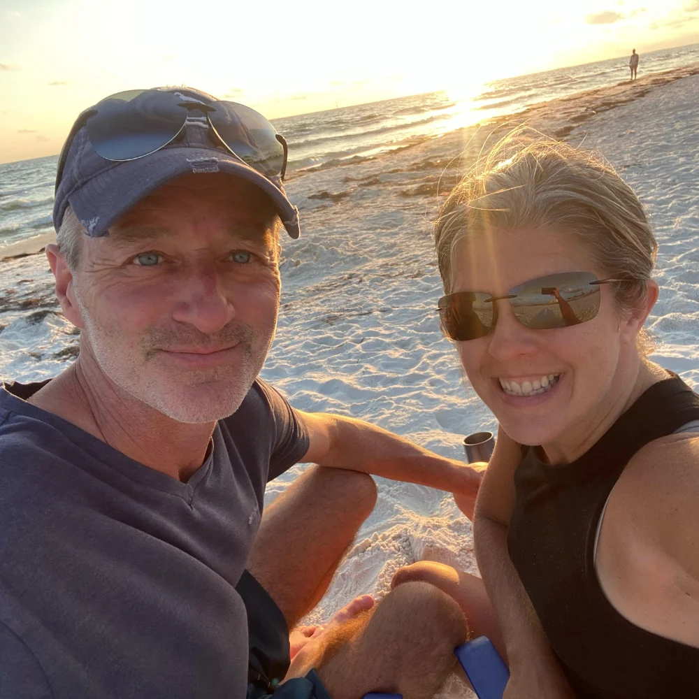 Two people sitting on a beach at sunset, waves touching their feet.