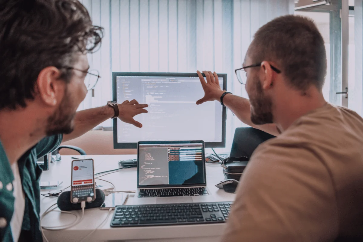 Two people discussing code on computer screens in an office setting.