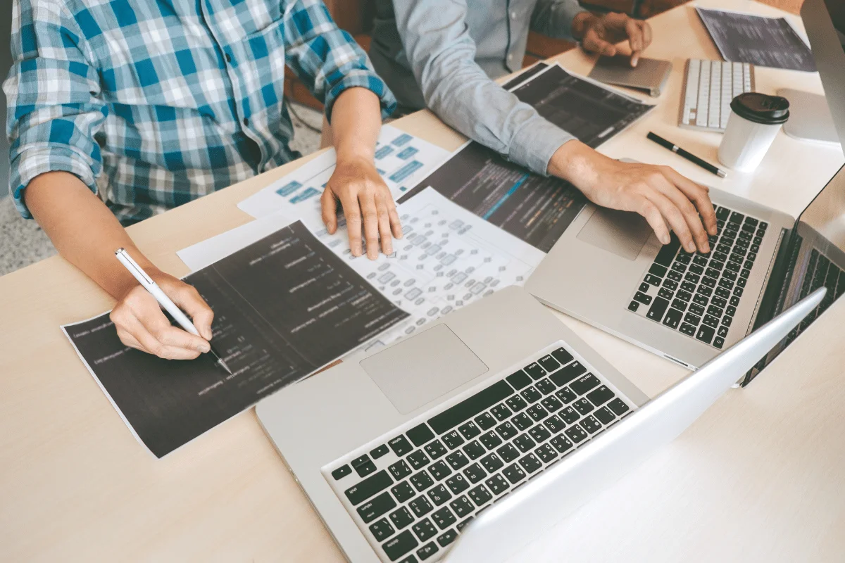Three individuals collaborating at a table with laptops, documents, and a coffee cup.